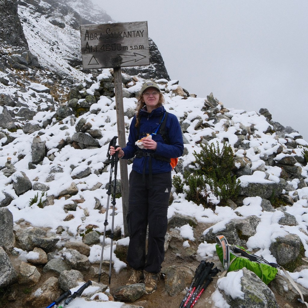 Image of Amy at the sign of the  Salkantay Trek peak, at an altitude of 4,600 metres. The background is icy and rocky. 